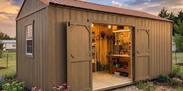 Garden shed with double doors open, revealing a well-organized workbench and tools inside, surrounded by blooming flowers in the yard at sunset.