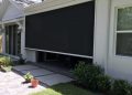 Backyard patio with a large black retractable shade screen extended over the seating area and sliding doors behind it.