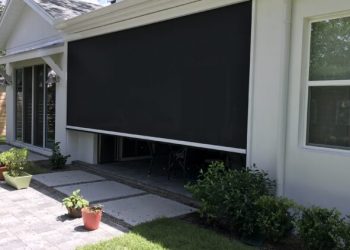 Backyard patio with a large black retractable shade screen extended over the seating area and sliding doors behind it.