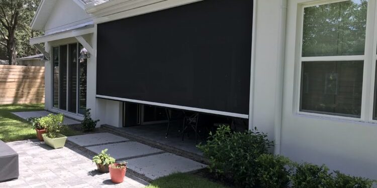 Backyard patio with a large black retractable shade screen extended over the seating area and sliding doors behind it.