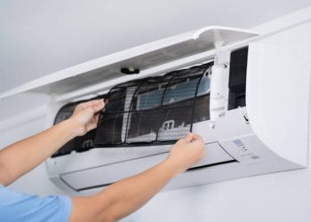 Person cleaning or replacing the filter inside a wall-mounted split air conditioner unit.