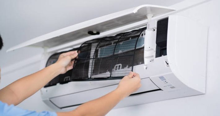Person cleaning or replacing the filter inside a wall-mounted split air conditioner unit.
